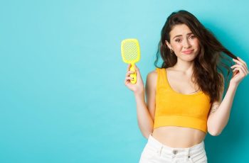 young-woman-disappointed-with-hair-loss-condition-showing-hair-brush-standing-upset-against-blue-bac